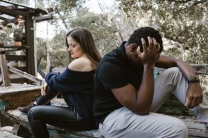 A couple sits back to back on a bench, depicting emotional conflict and loneliness.